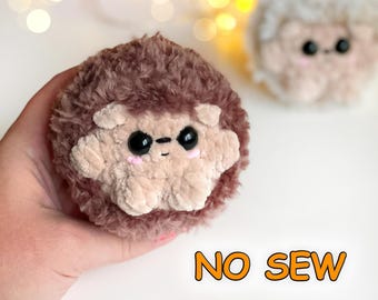 Può includere: Un peluche a forma di riccio marrone e beige con grandi occhi neri e guance rosa, caratterizzato da una consistenza soffice. Il testo NO SEW è visibile nell'angolo in basso a destra. Un secondo riccio di peluche più chiaro è visibile sullo sfondo.