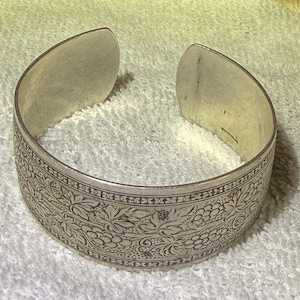 May include: A wide sterling silver cuff bracelet featuring an intricate engraved pattern of grape clusters and vine leaves. The interior of the band is clearly stamped with the text "MEX STERLING" indicating its composition and origin.