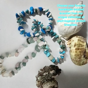 Può includere: Due braccialetti elastici realizzati con pietre irregolari levigate nei toni del blu, bianco e rosa pallido, disposti vicino a tre conchiglie. Il testo recita: Choose your favorite handmade beaded bracelet from our unique collection of shell-inspired stretch bracelets.