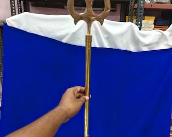 May include: A long, polished brass trident featuring a three-pronged head with a central point and two curved side blades. The metal staff has a smooth, cylindrical shaft that connects to the head with a decorative ring detail at the base.