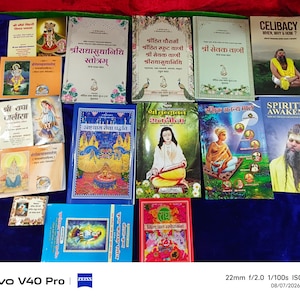 Może przedstawiać: Kolekcja czternastu książek z różnymi okładkami, zawierającymi ilustracje religijne, portrety osób oraz tekst w języku hindi i angielskim. Książki są ułożone w układzie siatki, prezentując różnorodne tytuły, takie jak Celibacy When, Why & How oraz Spiritual Awakening.