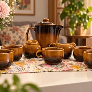 Op de afbeelding: Een keramische theeset bestaande uit een grote theepot met deksel, een suikerpot met deksel, een melkkannetje en vier bijpassende theekopjes. Elk stuk heeft een tweekleurig glazuur met een warme amberkleurige bovenkant en een donkerbruine basis.