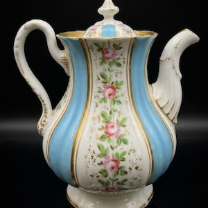 May include: A porcelain teapot featuring vertical light blue and white panels with gold trim. The white panels are decorated with hand-painted pink roses and green leaves. The teapot includes a matching lid with a finial, a curved handle, and a spout.
