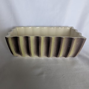 May include: A rectangular ceramic planter with a scalloped, fluted exterior. The outer surface features a gradient of muted olive green and dark brown vertical stripes, while the interior is finished in a smooth, solid off-white glaze.