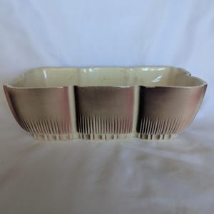 May include: A rectangular ceramic bowl with a scalloped edge and a cream-colored interior. The exterior features a gradient finish transitioning from a light cream base to a dark brown, metallic-toned rim, accented by vertical ribbed detailing.