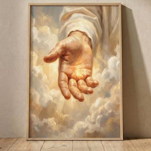 Könnte beinhalten: Ein gerahmter Wandkunstdruck, der ein realistisches Ölgemälde einer offenen Hand zeigt, die aus einer wirbelnden Weite aus goldenen und weißen Wolken nach vorne greift. Die Hand wird von einem warmen, strahlenden Licht aus der Mitte beleuchtet.