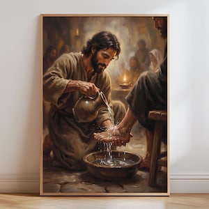 May include: A framed wall art print depicting a scene of a person with long dark hair and a beard kneeling while pouring water from a ceramic pitcher over another person's feet into a round basin, with other figures visible in the dim background.