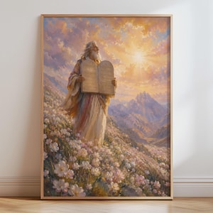 May include: A framed vertical wall art print depicting a bearded figure in flowing robes standing on a flower-covered mountainside. The figure holds two stone tablets towards a bright, golden sunrise in a cloudy sky above distant mountain peaks.