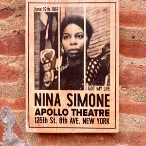 Può includere: Una targa rettangolare in legno con un ritratto in bianco e nero di Nina Simone. Il testo recita: June 19th 1961, I GOT MY LIFE, NINA SIMONE, APOLLO THEATRE, 125th St. 8th AVE. NEW YORK. Il ritratto è diviso in tre pannelli verticali.