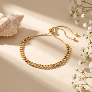 May include: A gold-toned curb chain bracelet featuring an adjustable sliding clasp mechanism with two small spherical beads at the ends of the thin, dangling chain extensions, creating a flexible and secure fit for the wrist.