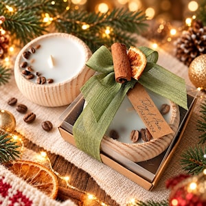 May include: Two round candles in light wood bowls with white wax and coffee beans. One candle is in a clear box with a green ribbon, a cinnamon stick, a dried orange slice, and a brown tag reading "Tilly & Aria 20.12.2024".