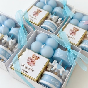 May include: A set of gift boxes containing light blue bubble candles, a carousel horse ornament, and a square chocolate bar with a label featuring a teddy bear illustration and the text Hosgeldin Seda, tied with a light blue sheer ribbon.
