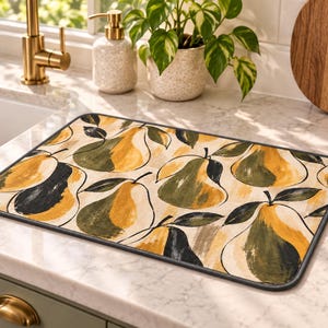 Peut inclure: Un tapis de séchage rectangulaire pour cuisine arborant un motif répétitif de poires stylisées dans des tons jaune moutarde, vert olive et noir sur fond crème, bordé d'une finition en tissu gris foncé.