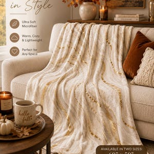 May include: A cream-colored throw blanket with wavy gold foil accents draped over a sofa. The text reads COZY UP in Style, Ultra Soft Microfiber, Warm, Cozy & Lightweight, Perfect for Any Space, and AVAILABLE IN TWO SIZES: 60" x 50" 80" x 60".