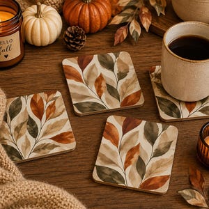 Pode incluir: Três porta-copos quadrados com uma estampa botânica em estilo aquarela de folhas de outono em tons de laranja queimado, verde sálvia e creme. Os porta-copos têm cantos arredondados e exibem um padrão repetitivo de folhagem em fundo claro.