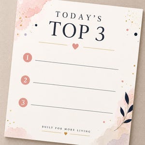 May include: A rectangular planner sheet with a cream background, featuring the text TODAY'S TOP 3 in dark blue. It includes three numbered pink circles, horizontal lines for writing, gold speckles, pink watercolor accents, and a small leaf illustration.