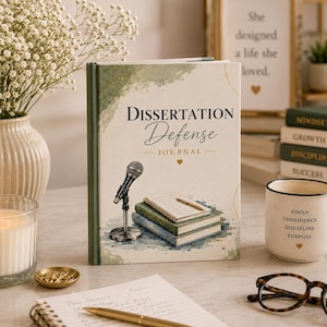 May include: A hardcover journal with a cream-colored cover featuring the text "DISSERTATION Defense JOURNAL" in black and gold. The cover illustration depicts a silver microphone standing next to a stack of three books with a pen on top.