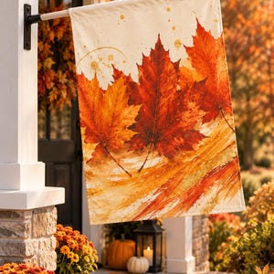 May include: A rectangular garden flag featuring a watercolour-style illustration of vibrant orange, red, and yellow maple leaves against a cream background. The design includes gold paint splatters and brushstroke textures across the fabric surface.