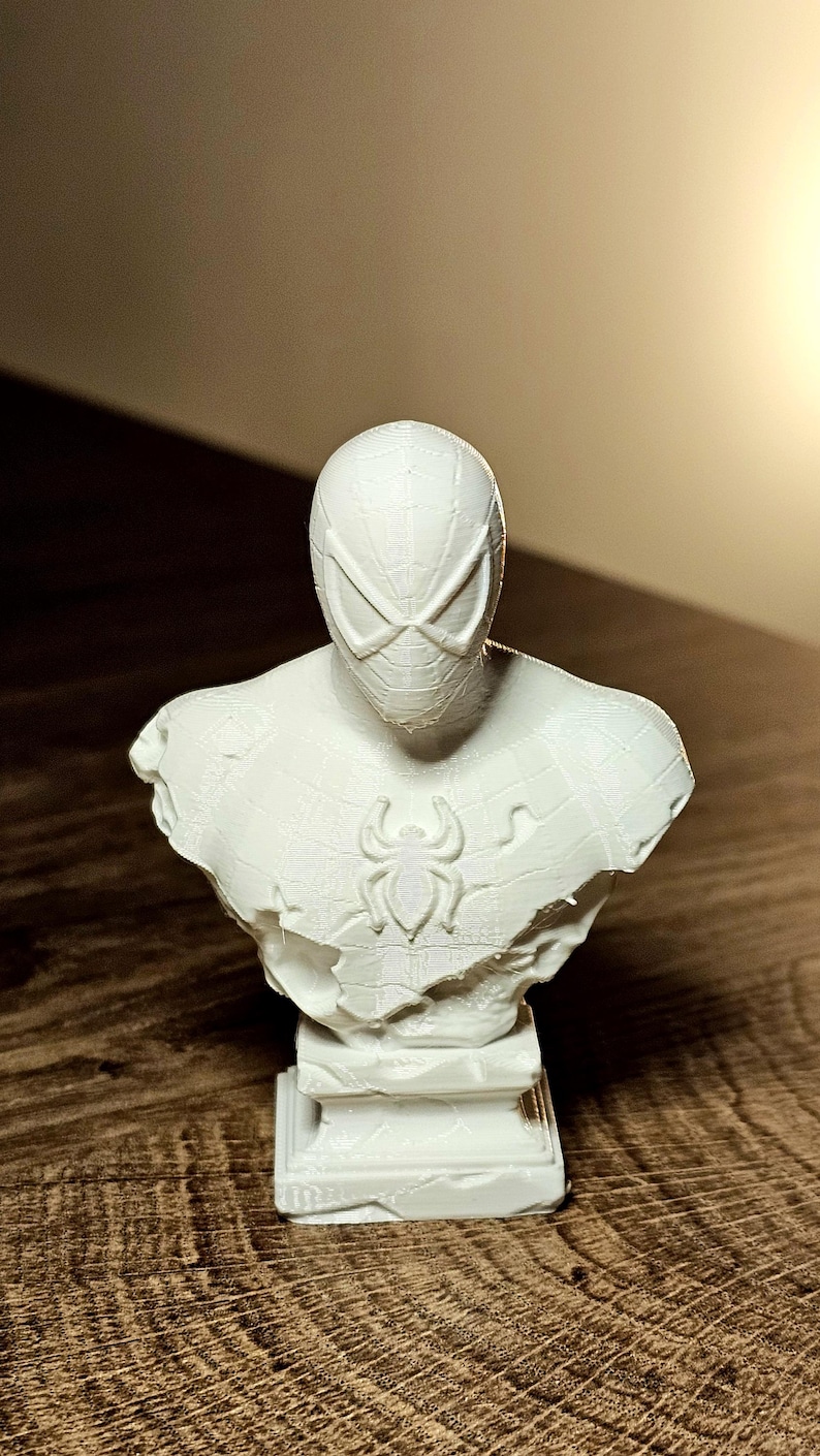 Op de afbeelding: Een witte buste van Spider-Man, met het masker en het borstembleem van het personage. De sculptuur heeft een getextureerd oppervlak en staat op een rechthoekige basis. Een verzamelobject.