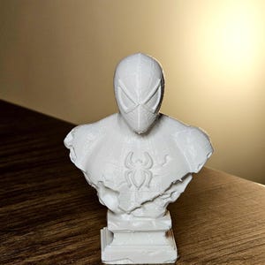 Op de afbeelding: Een witte buste van Spider-Man, met het masker en het borstembleem. De sculptuur is 3D-geprint en staat op een rechthoekige basis. De buste is een decoratief item.