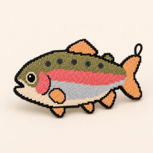 Op de afbeelding: Een visvormige patch gemaakt met punch needle borduurwerk en een zwarte omlijning. De vis heeft een olijfgroene rug met donkere stippen, een felroze horizontale streep, een lichtgrijze buik en perzikkleurige vinnen en een staart.