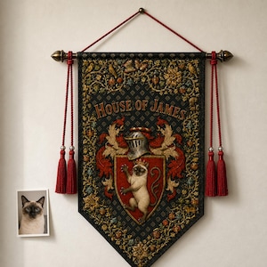 Może przedstawiać: Prostokątny baner ścienny z napisem HOUSE OF JAMES, srebrnym hełmem rycerskim i tarczą z ilustracją kota syjamskiego. Baner ma ciemne tło we wzory, złote kwiatowe obramowania oraz czerwone frędzle po obu stronach zawieszenia.