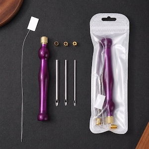 May include: A punch needle embroidery tool set featuring a purple ergonomic handle with a gold-toned metal tip, three interchangeable silver-toned needles of varying diameters, three small gold-toned rings, and a thin wire threader.