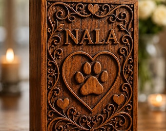 Puede incluir: Una caja rectangular de madera marrón oscuro con intrincados patrones tallados. El panel frontal muestra el nombre NALA en letras mayúsculas en relieve sobre un gran corazón tallado que contiene una huella de pata y dos corazones pequeños.