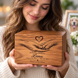 Peut inclure: Une urne rectangulaire en bois pour animal de compagnie avec une gravure laser représentant une main humaine tenant une patte de chien sous un cœur. Le texte indique : In Loving Memory, Luna, August 18, 2015 - May 02, 2025, Forever in Our Hearts.