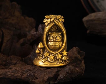 Può includere: Una piccola statuetta in metallo color oro a forma di tronco d'albero cavo. All'interno dell'apertura si trova un gufo dettagliato con grandi occhi. La base dell'albero è decorata con funghi scolpiti e foglie a forma di stella in rilievo.