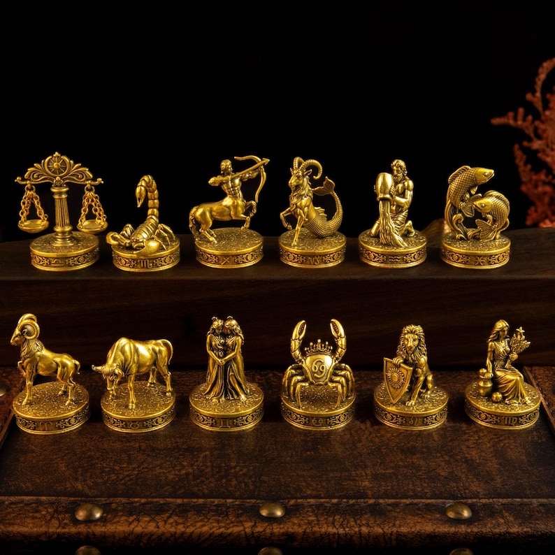 May include: A collection of twelve gold-toned metal zodiac figurines, each mounted on a circular base with embossed detailing. The set includes representations of Libra, Scorpio, Sagittarius, Capricorn, Aquarius, Pisces, Aries, Taurus, Gemini, Cancer, Leo, and Virgo.