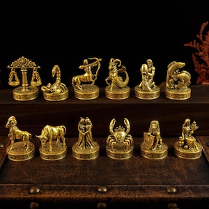 May include: A collection of twelve gold-toned metal zodiac figurines, each mounted on a circular base with engraved symbols. The set includes representations of Libra, Scorpio, Sagittarius, Capricorn, Aquarius, Pisces, Aries, Taurus, Gemini, Cancer, Leo, and Virgo.