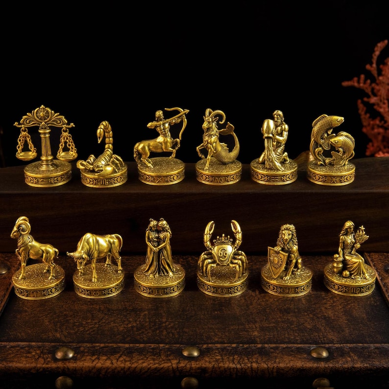 May include: A collection of twelve gold-toned metal zodiac figurines, each mounted on a circular base with engraved symbols. The set includes representations of Libra, Scorpio, Sagittarius, Capricorn, Aquarius, Pisces, Aries, Taurus, Gemini, Cancer, Leo, and Virgo.