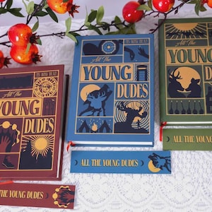 May include: Three hardcover books and two bookmarks with the text "All The Young Dudes". The books are in shades of blue, green, and burgundy, with illustrations of a wolf, deer, and other graphics. The bookmarks match the book designs.
