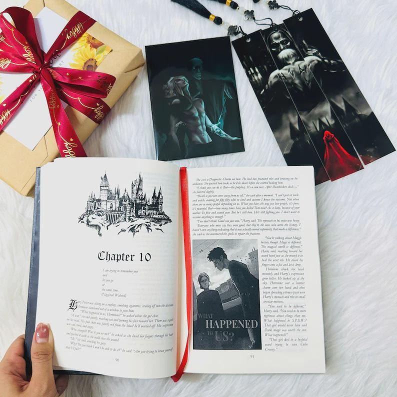 Pode incluir: Um livro aberto com o cap&iacute;tulo "Cap&iacute;tulo 10" e uma ilustra&ccedil;&atilde;o de um castelo. Um marcador e duas impress&otilde;es de arte s&atilde;o vis&iacute;veis. Uma caixa de presente embrulhada com uma fita vermelha tamb&eacute;m est&aacute; na imagem.