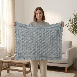 May include: A rectangular crochet blanket in a soft sage green color featuring a textured bobble stitch pattern throughout the center. The blanket is finished with a decorative scalloped edge border that frames the entire piece consistently.