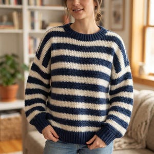 Peut inclure: Un pull à manches longues avec un motif à rayures horizontales bleu marine et crème. Le vêtement présente un col rond côtelé, des poignets côtelés et un ourlet côtelé, réalisé avec un point de tricot texturé sur le corps et les manches.