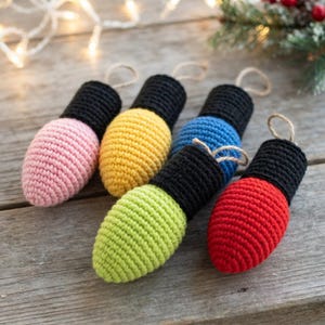 May include: Five crochet ornaments shaped like vintage light bulbs, each featuring a colorful bulb base in pink, yellow, blue, lime green, or red, topped with a black crocheted cap and a small jute twine loop for hanging on a tree.