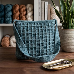 May include: A teal blue crochet shoulder bag featuring a raised waffle stitch pattern throughout the body and a wide strap. The bag is constructed with a textured grid design and has a square silhouette with a consistent color tone throughout.