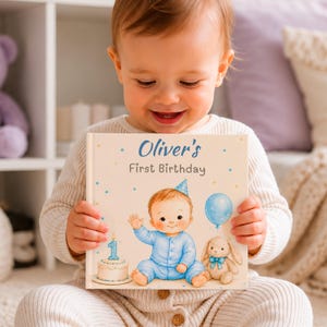 Puede incluir: Un libro de tapa dura cuadrado titulado Oliver's First Birthday. La portada presenta una ilustración de un bebé en pijama azul con un gorro de fiesta, un pastel de cumpleaños con una vela del número uno y un conejo de peluche.