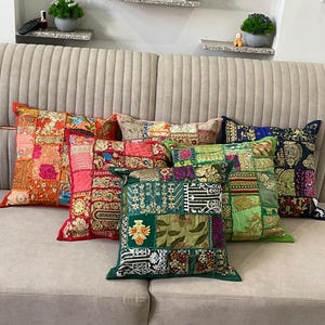 Könnte beinhalten: Eine Sammlung von fünf quadratischen Zierkissen mit einem Patchwork-Design aus verschiedenen bestickten Stoffen in leuchtenden Farben wie Orange, Rot, Grün und Dunkelblau, die jeweils komplexe Muster und dekorative Stickereidetails aufweisen.