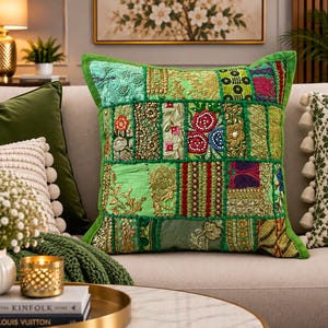 Könnte beinhalten: Ein quadratisches Dekokissen mit einem Patchwork-Design aus verschiedenen grünen Stoffbahnen. Die Oberfläche ist mit aufwendigen Goldstickereien, Perlenarbeiten und floralen Mustern in verschiedenen Rosa-, Blau- und Rottönen verziert.