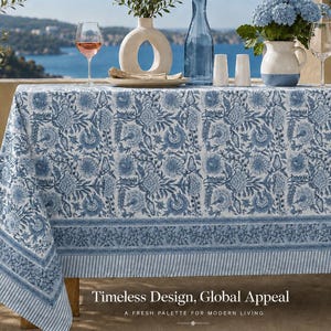 May include: A rectangular tablecloth featuring a blue and white floral block print pattern with a decorative border and striped edge. The fabric displays intricate botanical motifs across the surface. Text at the bottom reads: Timeless Design, Global Appeal, A FRESH PALETTE FOR MODERN LIVING.