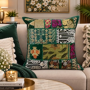 May include: A square throw pillow featuring a patchwork design of various green fabrics. The surface is decorated with intricate embroidery, gold metallic thread accents, floral patterns, and small beadwork in shades of magenta, orange, and white.