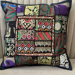 May include: A square throw pillow featuring a patchwork design of various embroidered fabric panels. The surface displays a mix of vibrant colors including red, green, purple, gold, and black, with intricate floral, geometric, and mirror-like patterns.