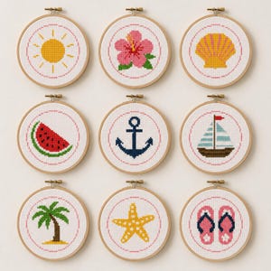 May include: Nine circular wooden embroidery hoops containing white fabric with cross-stitch designs. The patterns include a yellow sun, pink hibiscus flower, yellow seashell, watermelon slice, blue anchor, sailboat, palm tree, yellow starfish, and pink flip-flops.