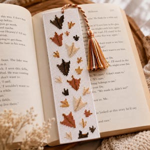 May include: A rectangular white bookmark featuring a cross-stitch pattern of various bird footprints in shades of brown, tan, and cream. The bookmark is finished with a braided cord and a multi-colored tassel in matching earth tones.