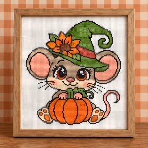 May include: A framed cross-stitch embroidery featuring a grey mouse with large pink-lined ears wearing a green pointed hat adorned with an orange sunflower. The mouse is holding a bright orange pumpkin. The design is set against a white grid fabric.