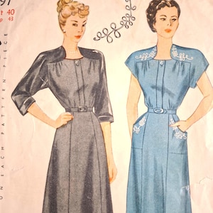 May include: A vintage sewing pattern envelope featuring illustrations of two dresses. One is a dark charcoal grey dress with three-quarter sleeves and a belt. The other is a light blue dress with short sleeves, white decorative embroidery, and a belt.
