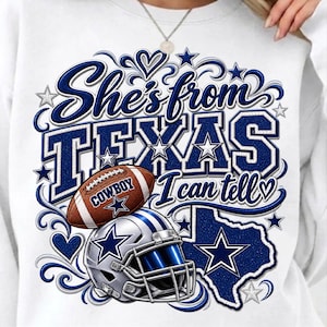 May include: A white sweatshirt featuring a blue graphic design with the text "She's from TEXAS I can tell". The design includes a brown football with the word "COWBOY", a silver and blue football helmet, a map of Texas, and various star accents.